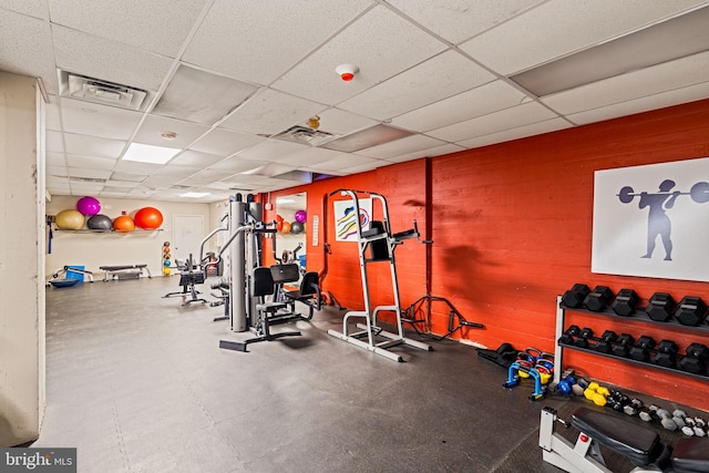 workout area featuring visible vents, wooden walls, and a drop ceiling