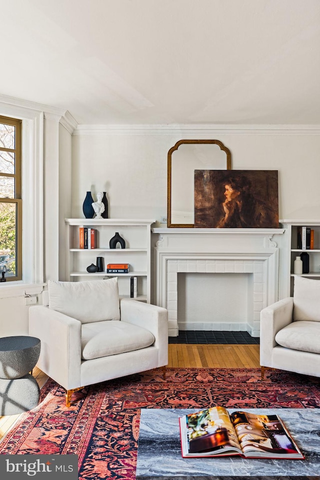 living area featuring a brick fireplace, crown molding, and wood finished floors