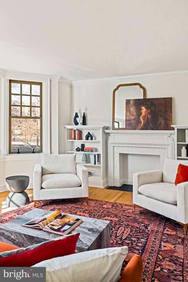 living area featuring a fireplace, ornamental molding, and wood finished floors