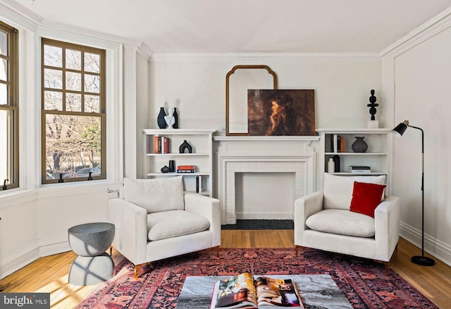 sitting room with ornamental molding, a fireplace with flush hearth, and wood finished floors