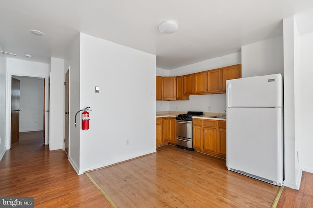 709 E Passyunk Ave, Philadelphia, PA 19147 - kitchen with light countertops, brown cabinetry, freestanding refrigerator, stainless steel gas stove, and light wood-type flooring