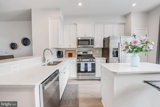 kitchen with light stone counters, stainless steel appliances, a peninsula, a sink, and light wood finished floors