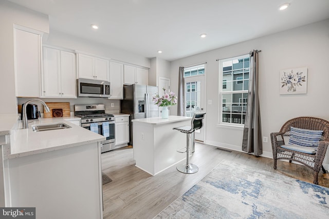 kitchen featuring a kitchen island, a sink, white cabinets, appliances with stainless steel finishes, and light wood finished floors