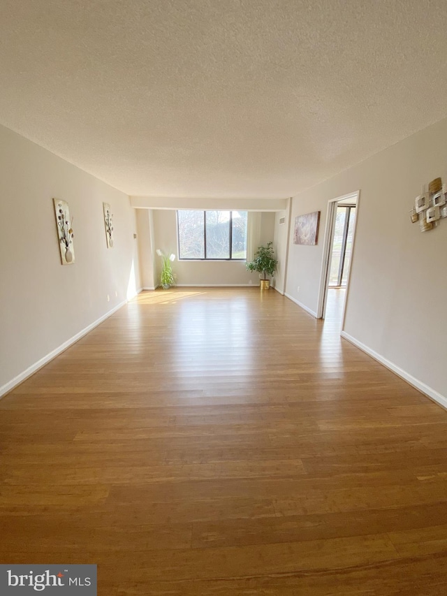 unfurnished living room with a textured ceiling, wood finished floors, and baseboards