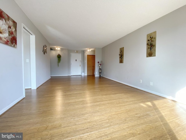 empty room with a textured ceiling, light wood-type flooring, and baseboards