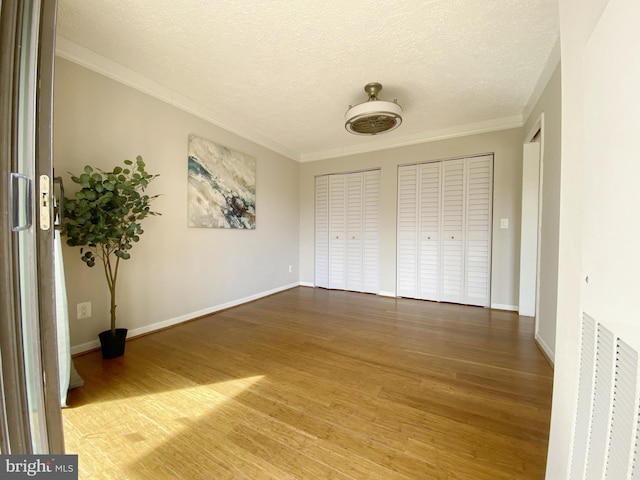 unfurnished bedroom with a textured ceiling, light wood-style floors, baseboards, multiple closets, and crown molding