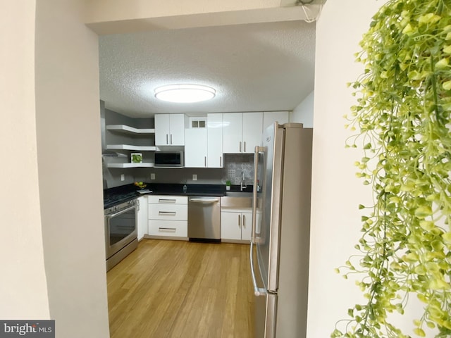 kitchen featuring dark countertops, light wood-type flooring, appliances with stainless steel finishes, and white cabinets