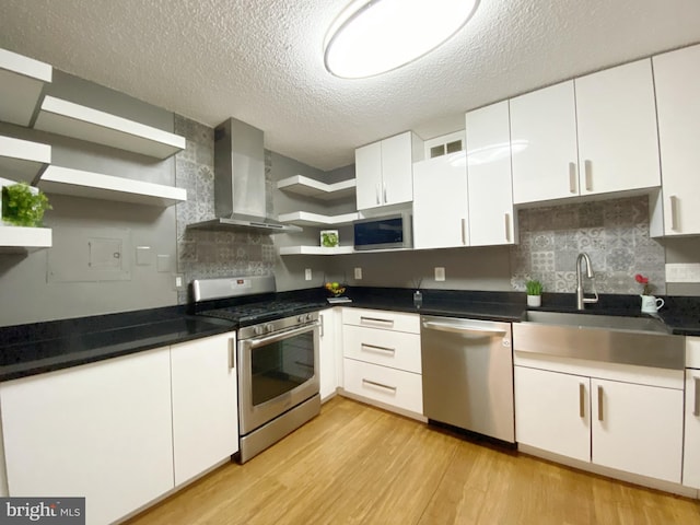 kitchen featuring light wood finished floors, open shelves, stainless steel appliances, white cabinets, and wall chimney range hood