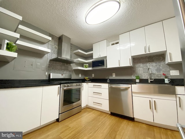 kitchen featuring open shelves, appliances with stainless steel finishes, light wood-style floors, white cabinets, and wall chimney range hood