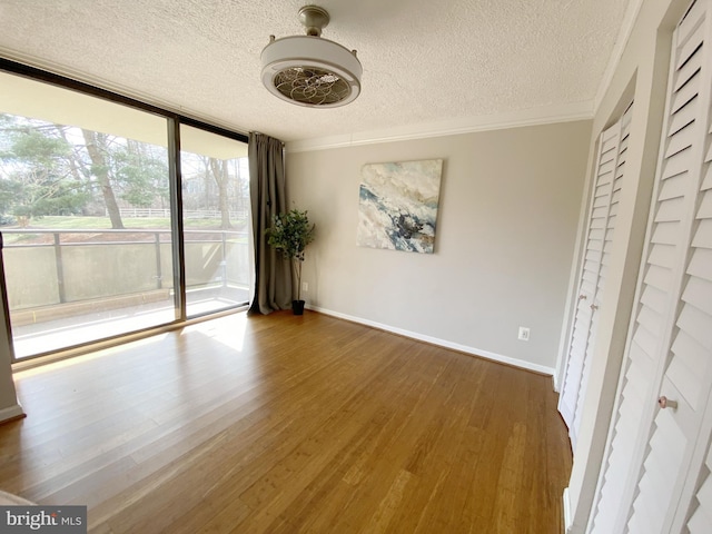 interior space with a textured ceiling, wood finished floors, baseboards, ornamental molding, and expansive windows