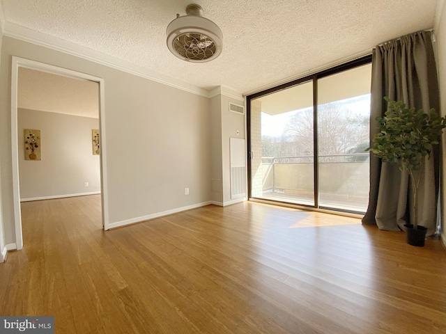 unfurnished room featuring wood finished floors, visible vents, baseboards, floor to ceiling windows, and crown molding