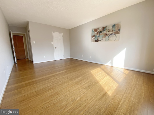 unfurnished living room featuring a textured ceiling, baseboards, and wood finished floors