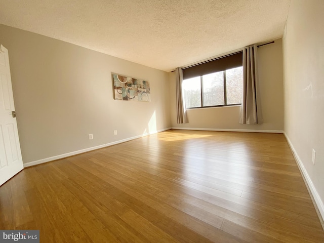 empty room featuring a textured ceiling, baseboards, and wood finished floors