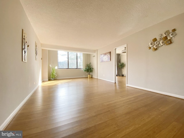 unfurnished room with a textured ceiling, baseboards, and wood finished floors