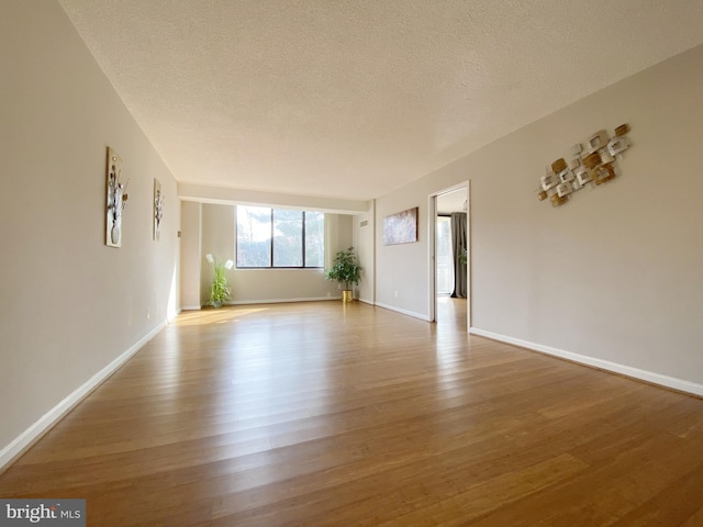 empty room with a textured ceiling, wood finished floors, and baseboards