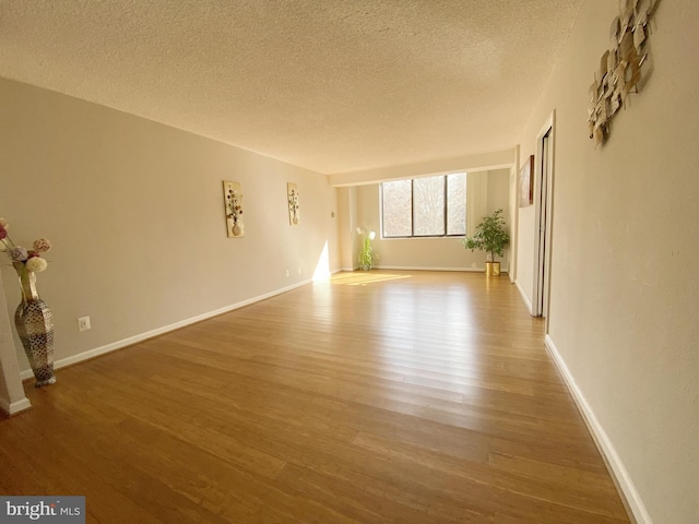 unfurnished living room with a textured ceiling, wood finished floors, and baseboards