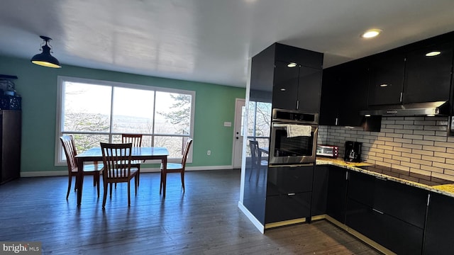 kitchen with black electric cooktop, under cabinet range hood, oven, dark cabinets, and decorative backsplash