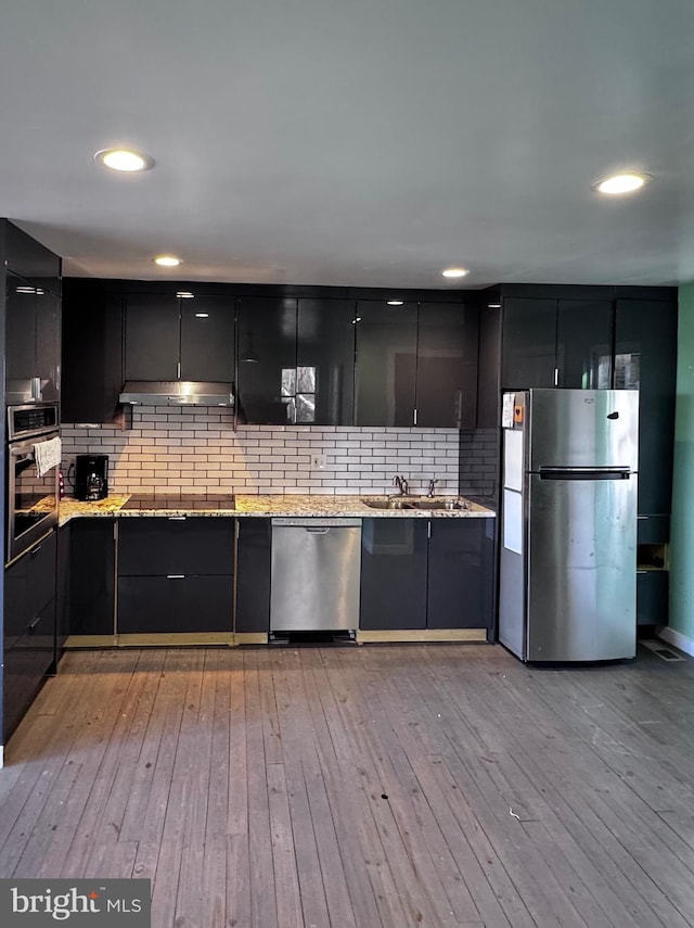 kitchen featuring stainless steel appliances, under cabinet range hood, light wood finished floors, and modern cabinets