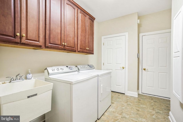 washroom featuring cabinet space, baseboards, separate washer and dryer, and a sink