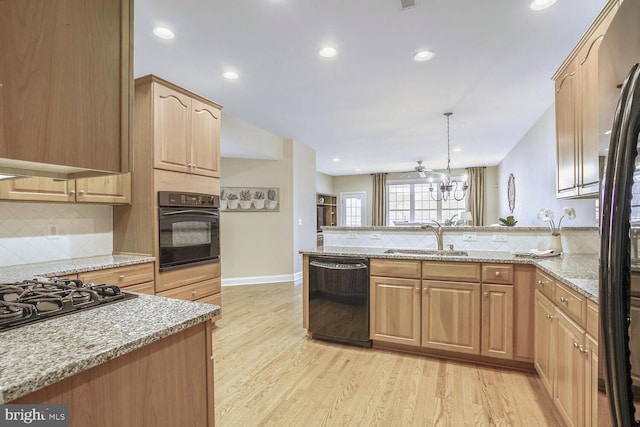 kitchen with light stone counters, light wood-style flooring, a peninsula, a sink, and black appliances