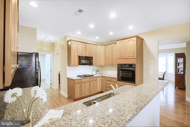 kitchen with light stone counters, visible vents, light brown cabinets, a sink, and black appliances