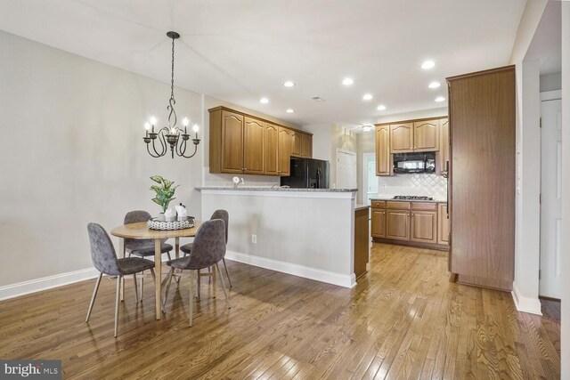 kitchen with light wood-style flooring, decorative backsplash, black appliances, a peninsula, and baseboards