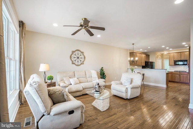 living area with ceiling fan with notable chandelier, hardwood / wood-style flooring, visible vents, and recessed lighting