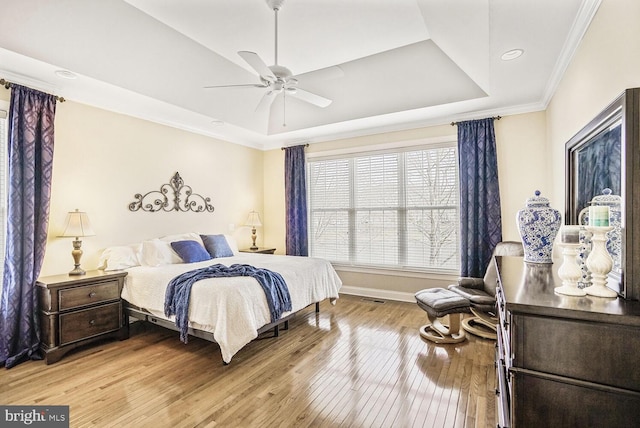 bedroom featuring light wood-style flooring, baseboards, a raised ceiling, and crown molding