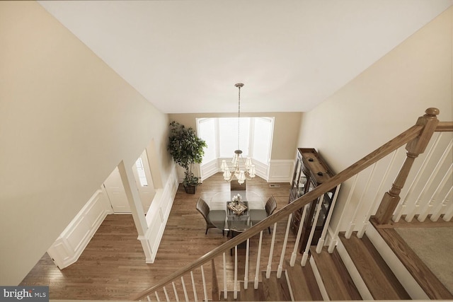 stairway featuring a decorative wall, wainscoting, wood finished floors, and a notable chandelier