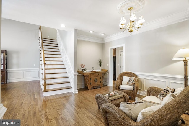 sitting room with a decorative wall, a notable chandelier, wood finished floors, ornamental molding, and stairway