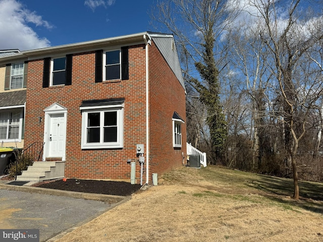 view of front facade featuring brick siding, central air condition unit, and a front yard