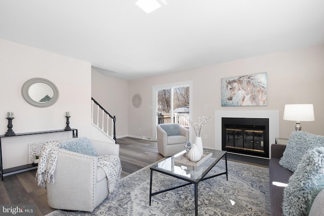 living area featuring stairway, wood finished floors, baseboards, and a glass covered fireplace