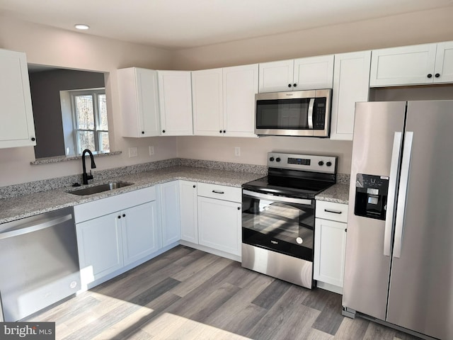 kitchen with light stone countertops, light wood-type flooring, stainless steel appliances, white cabinetry, and a sink