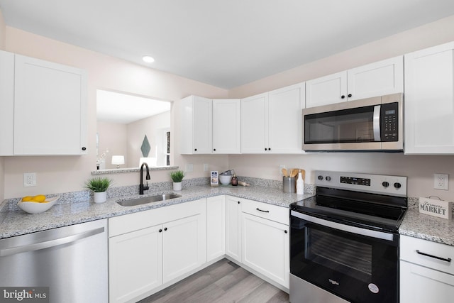 kitchen with light stone counters, light wood-style flooring, appliances with stainless steel finishes, white cabinets, and a sink