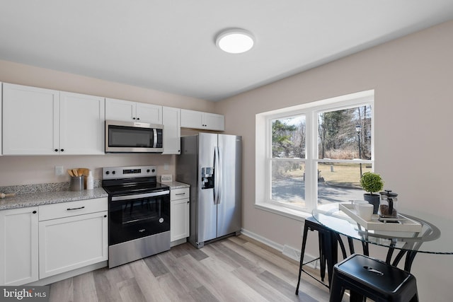 kitchen featuring white cabinets, light wood finished floors, appliances with stainless steel finishes, and light stone counters