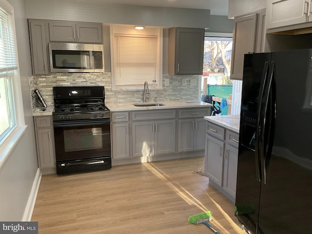 kitchen featuring black appliances, decorative backsplash, light wood finished floors, and a sink