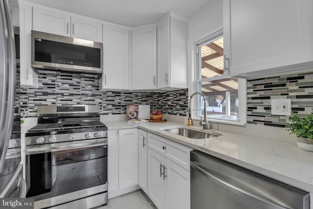 kitchen featuring stainless steel appliances, a sink, white cabinets, marble finish floor, and tasteful backsplash