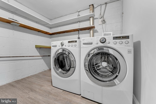 clothes washing area with laundry area, separate washer and dryer, wood finished floors, and concrete block wall