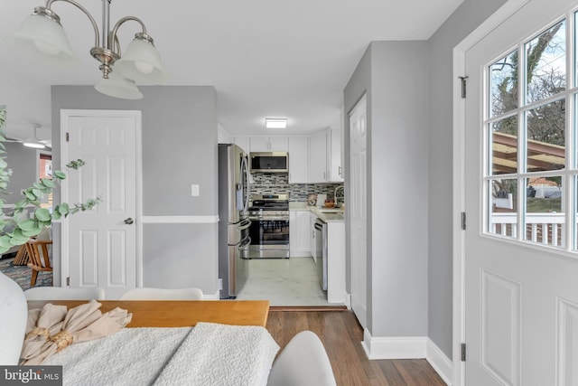 kitchen featuring wood finished floors, white cabinets, light countertops, appliances with stainless steel finishes, and tasteful backsplash