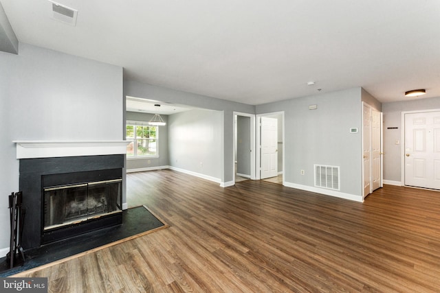 unfurnished living room featuring a glass covered fireplace, visible vents, baseboards, and wood finished floors