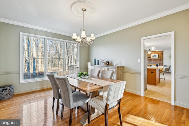 dining room with ornamental molding, a chandelier, baseboards, and light wood finished floors