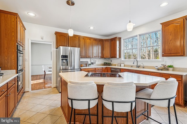 kitchen with a sink, a kitchen island, light countertops, appliances with stainless steel finishes, and decorative light fixtures