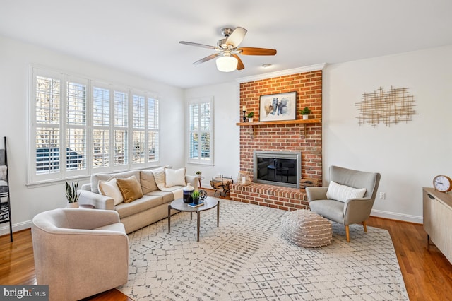 living room with ceiling fan, a brick fireplace, wood finished floors, and baseboards