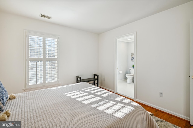 bedroom featuring ensuite bath, wood finished floors, visible vents, and baseboards