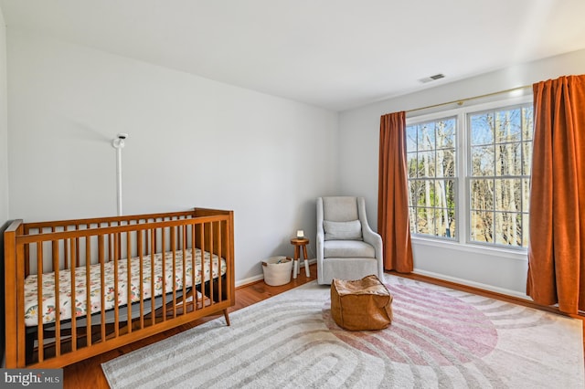 bedroom with a nursery area, visible vents, baseboards, and wood finished floors