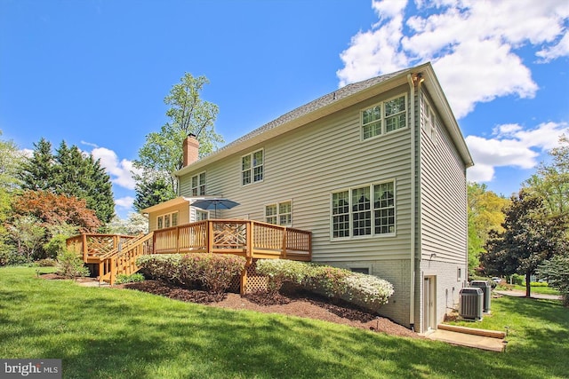 rear view of property featuring a chimney, a lawn, a deck, and central AC unit