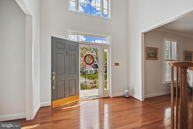 foyer with light wood-style floors, a high ceiling, ornamental molding, and baseboards