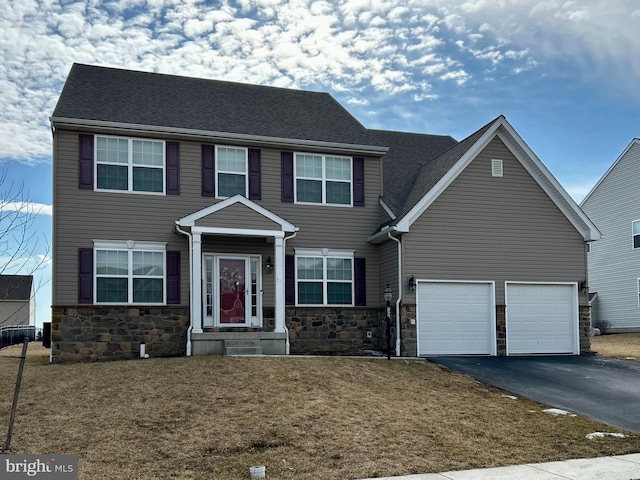 colonial home with aphalt driveway, stone siding, and an attached garage