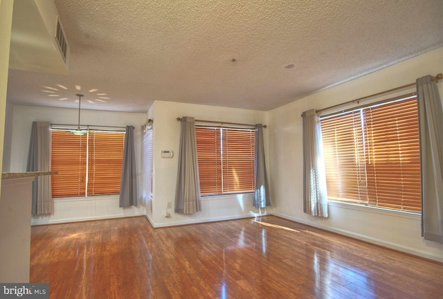 unfurnished room featuring wood-type flooring, visible vents, baseboards, and a textured ceiling