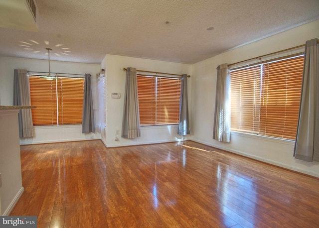 unfurnished room with wood-type flooring, visible vents, a textured ceiling, and baseboards